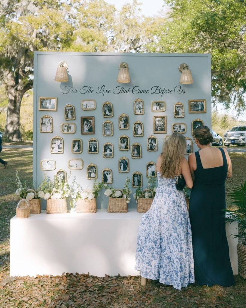 Two women viewing a nostalgic photo display featuring many framed vintage family photographs outdoors.