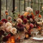 Floral wedding centerpieces with burgundy and peach dahlias on a decorated wooden dining table.