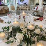 Clear glass cylinder vases with floating candles surrounded by white roses and greenery on a table.
