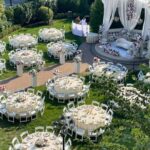 Aerial view of round wedding tables with white linens set in a lush green garden estate.