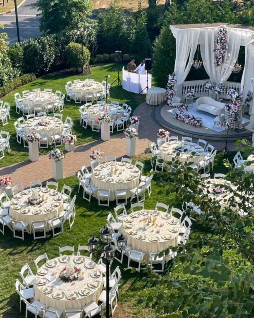 Aerial view of round wedding tables with white linens set in a lush green garden estate.