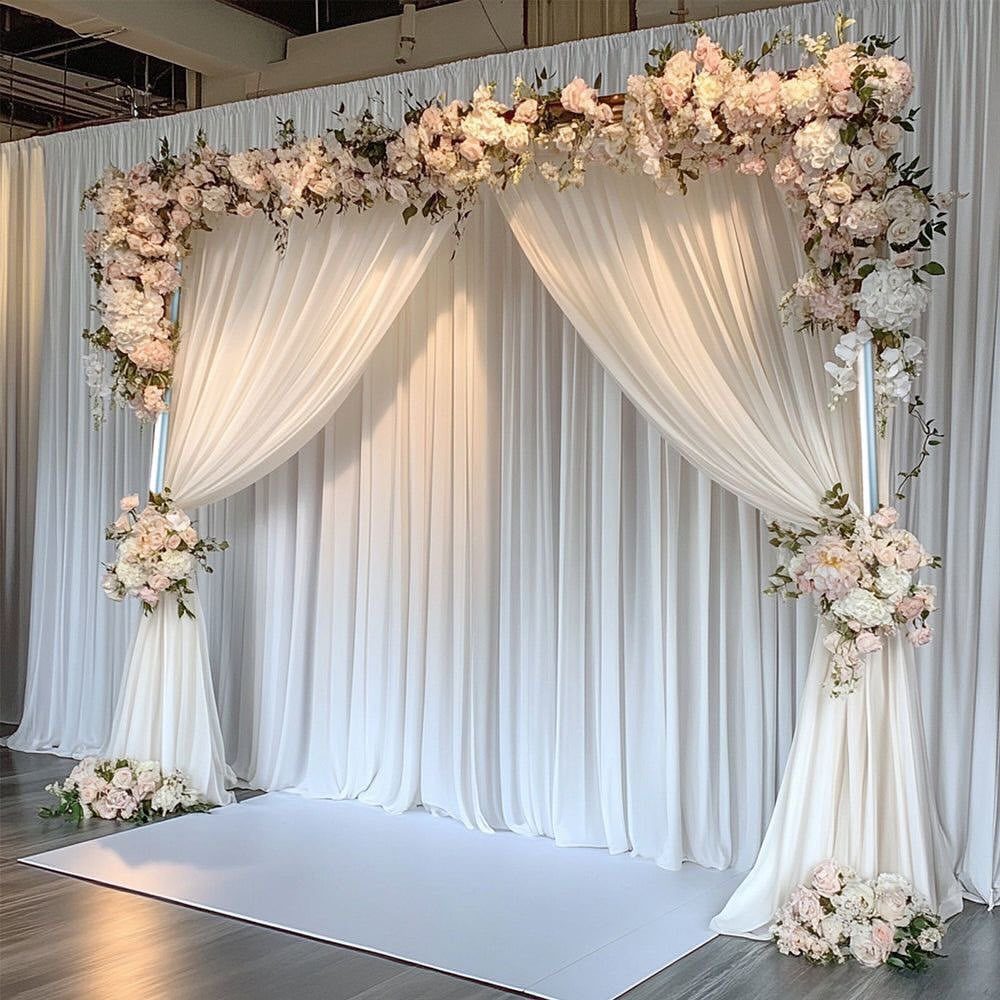 A floral wedding arch with white fabric drapes against a backdrop of white curtains.
