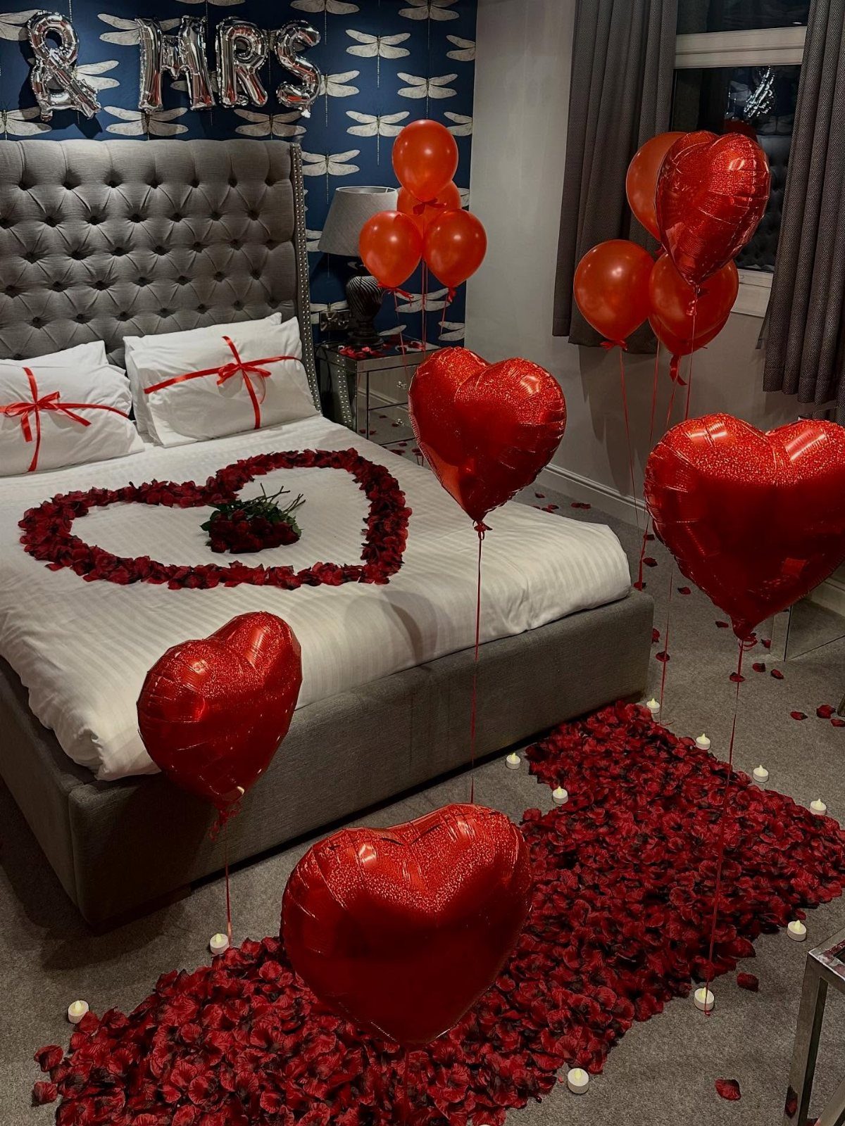 Red heart balloons and rose petals decorate a bedroom for a wedding celebration.