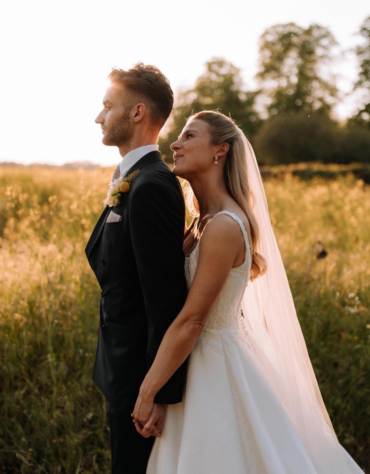 A bride and groom holding hands in a golden field during sunset.