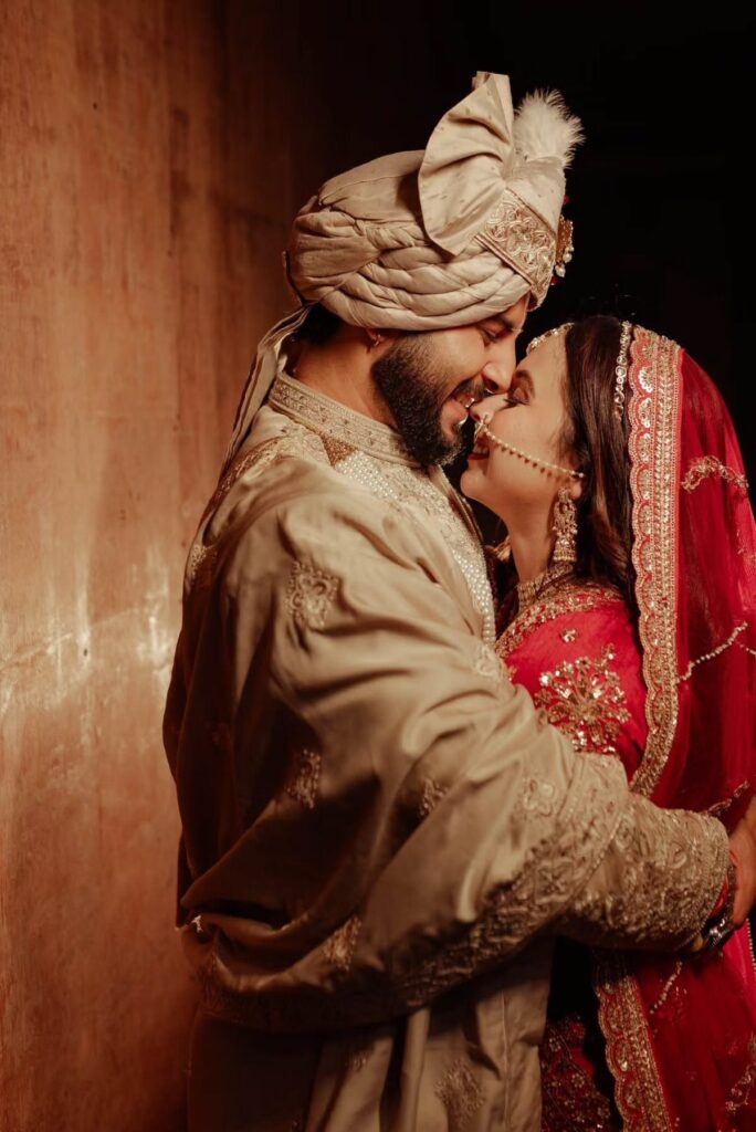 An Indian bride and groom in traditional wedding attire smiling while embracing closely.