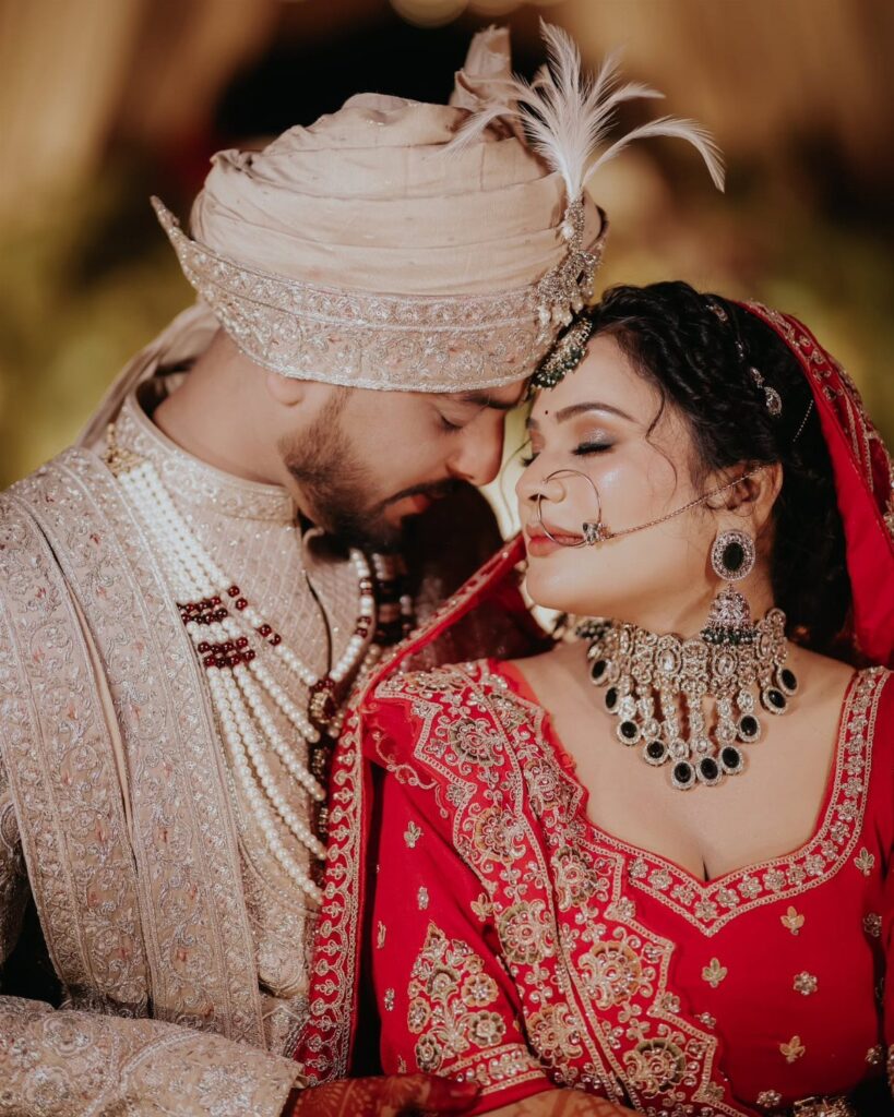 An Indian bride and groom in traditional wedding attire posing closely with eyes closed.