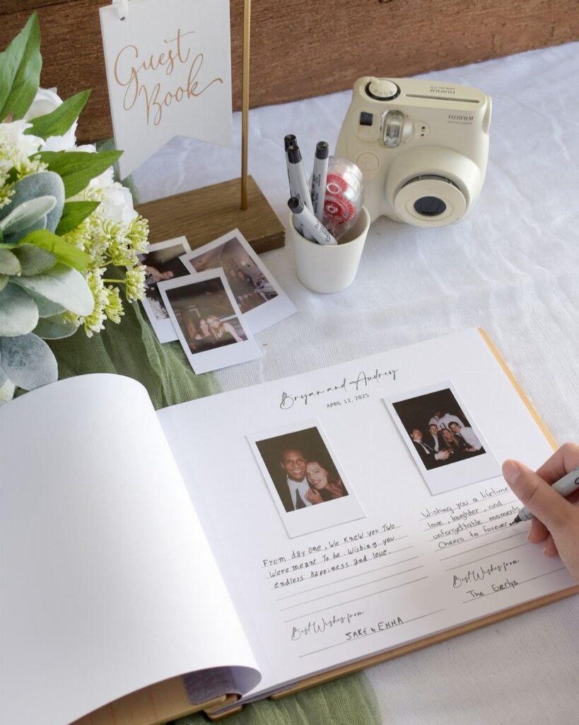 An open wedding guest book with Polaroid photos and handwritten notes on a white table.
