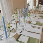 Small glass bud vases with colorful wildflowers and tall blue candles on a wedding reception table.